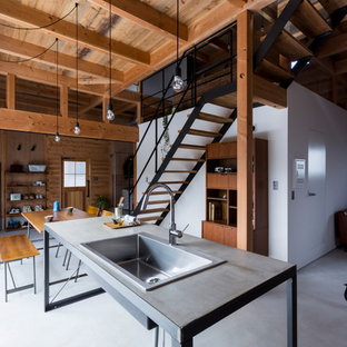 Ejemplo de cocina lineal, industrial, de tamaño medio, abierta, con suelo de cemento, fregadero integrado, armarios abiertos, puertas de armario en acero inoxidable, encimera de cemento, salpicadero blanco, salpicadero de ladrillos, electrodomésticos negros, una isla, suelo gris y encimeras grises