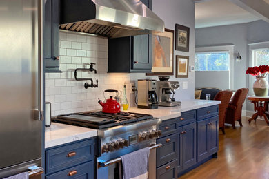 サンフランシスコにあるお手頃価格の中くらいなミッドセンチュリースタイルのおしゃれなキッチン (エプロンフロントシンク、青いキャビネット、クオーツストーンカウンター、白いキッチンパネル、サブウェイタイルのキッチンパネル、シルバーの調理設備、無垢フローリング、茶色い床、白いキッチンカウンター、フラットパネル扉のキャビネット) の写真