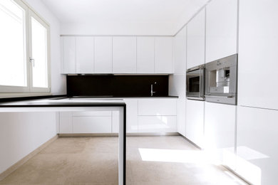 Foto di una piccola cucina minimalista con ante a filo, ante bianche, paraspruzzi nero, elettrodomestici in acciaio inossidabile, pavimento con piastrelle in ceramica, pavimento beige e top nero