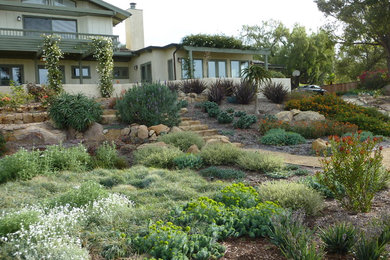 Photo of a mid-sized mediterranean front yard full sun xeriscape for summer in Santa Barbara with a retaining wall and natural stone pavers.