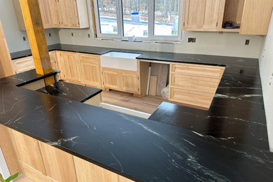 Example of a large cottage u-shaped eat-in kitchen design in Boston with a farmhouse sink, recessed-panel cabinets, medium tone wood cabinets, soapstone countertops, black backsplash, ceramic backsplash, no island and black countertops