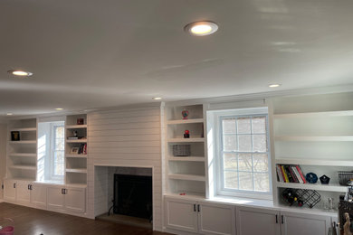 Example of a large minimalist enclosed family room library design in New York with white walls, a shiplap fireplace and a media wall