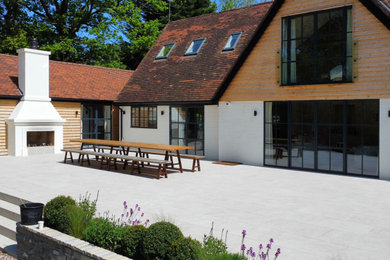 This is an example of a large and white two floor rear house exterior in Surrey with wood cladding and a red roof.