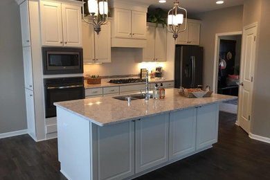 Example of a mid-sized classic single-wall dark wood floor and brown floor enclosed kitchen design in Orange County with a double-bowl sink, raised-panel cabinets, white cabinets, granite countertops, white backsplash, porcelain backsplash, stainless steel appliances and an island
