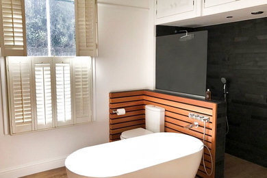 Photo of a large contemporary kids bathroom in London with a freestanding tub, an open shower, a two-piece toilet, black tile, slate, white walls, light hardwood floors, brown floor and an open shower.