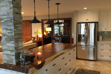This is an example of a mid-sized transitional l-shaped open plan kitchen in Kansas City with shaker cabinets, white cabinets, wood benchtops, green splashback, subway tile splashback, stainless steel appliances, porcelain floors, with island and beige floor.