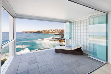 This is an example of a large contemporary balcony in Sydney with a roof extension and glass railing.