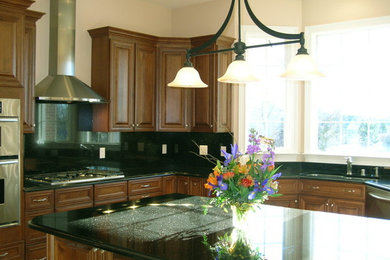 Example of a mid-sized classic l-shaped enclosed kitchen design in Milwaukee with a double-bowl sink, raised-panel cabinets, dark wood cabinets, granite countertops, black backsplash, stone slab backsplash, stainless steel appliances and an island