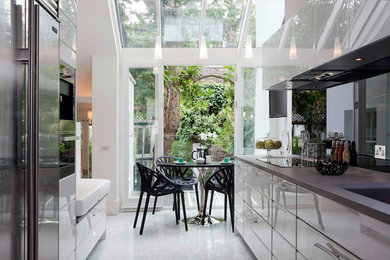 Design ideas for a medium sized modern galley kitchen/diner in London with flat-panel cabinets, glass sheet splashback, a submerged sink, white cabinets, quartz worktops, black splashback, stainless steel appliances, marble flooring and no island.