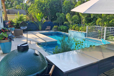 Ejemplo de piscina marinera de tamaño medio en forma de L en patio trasero con paisajismo de piscina y adoquines de piedra natural