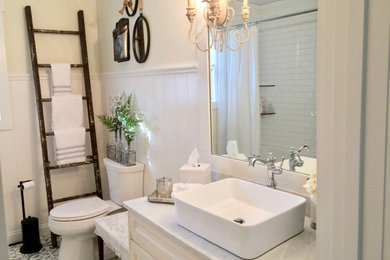 Example of a mid-sized farmhouse white tile and subway tile cement tile floor, blue floor and single-sink drop-in bathtub design in Cincinnati with yellow cabinets, a two-piece toilet, yellow walls, a vessel sink, marble countertops and gray countertops