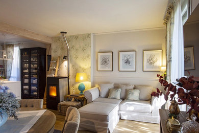 Diseño de sala de estar abierta clásica de tamaño medio con paredes beige, suelo de madera clara, estufa de leña, televisor colgado en la pared y papel pintado