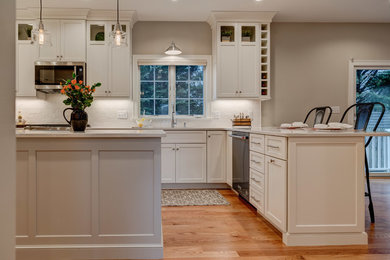 Inspiration for a large transitional u-shaped eat-in kitchen in Boston with an undermount sink, shaker cabinets, white cabinets, quartz benchtops, white splashback, porcelain splashback, stainless steel appliances, medium hardwood floors, with island, brown floor and white benchtop.
