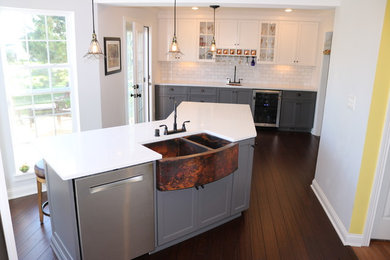 Inspiration for a mid-sized transitional dark wood floor and brown floor kitchen remodel in Louisville with a farmhouse sink, shaker cabinets, gray cabinets, quartz countertops, white backsplash, subway tile backsplash, stainless steel appliances, an island and white countertops