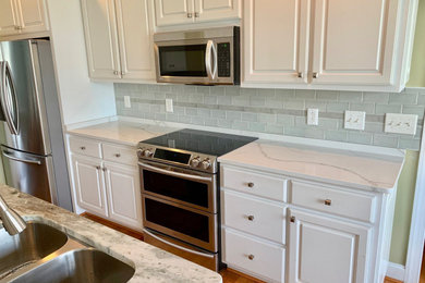 Mid-sized beach style medium tone wood floor eat-in kitchen photo in Wilmington with a double-bowl sink, raised-panel cabinets, white cabinets, green backsplash, porcelain backsplash, stainless steel appliances and an island