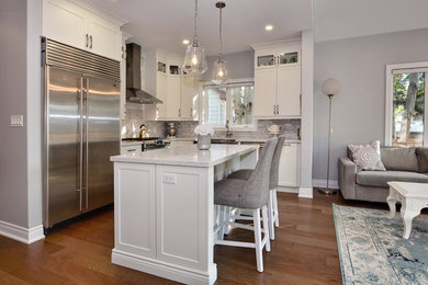 Eat-in kitchen - mid-sized transitional l-shaped medium tone wood floor and brown floor eat-in kitchen idea in Toronto with a farmhouse sink, shaker cabinets, white cabinets, quartz countertops, gray backsplash, marble backsplash, stainless steel appliances, an island and white countertops