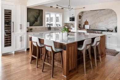 Eat-in kitchen - large transitional l-shaped medium tone wood floor and brown floor eat-in kitchen idea in Philadelphia with an undermount sink, shaker cabinets, white cabinets, quartzite countertops, beige backsplash, stone slab backsplash, paneled appliances, an island and beige countertops