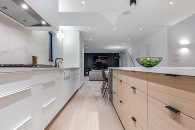 Inspiration for a large contemporary eat-in kitchen in Vancouver with a drop-in sink, flat-panel cabinets, white cabinets, white splashback, panelled appliances, with island, brown floor and white benchtop.