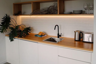 Design ideas for a mid-sized beach style galley eat-in kitchen with a drop-in sink, recessed-panel cabinets, white cabinets, wood benchtops, white splashback, subway tile splashback, stainless steel appliances, concrete floors, no island and multi-coloured floor.