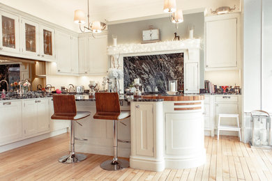 Inspiration for a mid-sized traditional l-shaped eat-in kitchen in Glasgow with granite benchtops, with island, a double-bowl sink, flat-panel cabinets, light wood cabinets, white splashback, timber splashback, panelled appliances, light hardwood floors and brown floor.