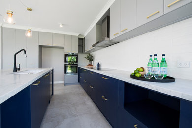 Design ideas for a large contemporary galley eat-in kitchen in Perth with a double-bowl sink, beaded inset cabinets, blue cabinets, marble benchtops, white splashback, ceramic splashback, black appliances, with island, porcelain floors, grey floor and white benchtop.