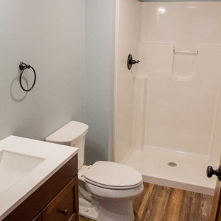 Diseño de cuarto de baño infantil, de estilo americano, pequeño, con armarios con paneles con relieve, puertas de armario de madera oscura, ducha empotrada, sanitario de dos piezas, paredes azules, suelo laminado, lavabo integrado, encimera de acrílico, suelo marrón y ducha abierta
