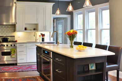 This is an example of a large transitional l-shaped eat-in kitchen in New York with an undermount sink, shaker cabinets, dark wood cabinets, quartz benchtops, white splashback, porcelain splashback, stainless steel appliances, medium hardwood floors, with island, brown floor and white benchtop.