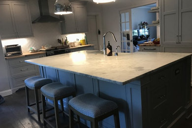 Inspiration for a mid-sized transitional l-shaped medium tone wood floor open concept kitchen remodel in Richmond with a farmhouse sink, beaded inset cabinets, gray cabinets, marble countertops, white backsplash, ceramic backsplash, stainless steel appliances and an island