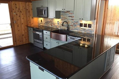 Mid-sized country l-shaped bamboo floor open concept kitchen photo in Indianapolis with a farmhouse sink, recessed-panel cabinets, green cabinets, granite countertops, multicolored backsplash, stone tile backsplash, colored appliances and a peninsula