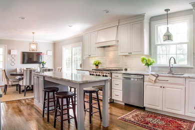 Transitional medium tone wood floor and brown floor open concept kitchen photo in Other with an undermount sink, raised-panel cabinets, white cabinets, granite countertops, gray backsplash, ceramic backsplash, stainless steel appliances and an island