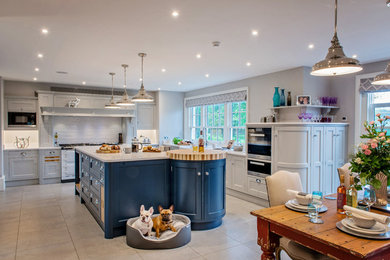 Large traditional open plan kitchen in Surrey with a farmhouse sink, shaker cabinets, blue cabinets, quartzite benchtops, white splashback, ceramic splashback, stainless steel appliances, porcelain floors, with island and grey floor.