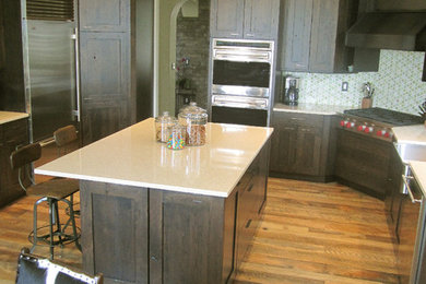 Open concept kitchen - large transitional u-shaped medium tone wood floor open concept kitchen idea in Denver with a farmhouse sink, shaker cabinets, dark wood cabinets, quartz countertops, green backsplash, glass tile backsplash, stainless steel appliances and an island