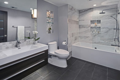 Design ideas for a small contemporary bathroom in Orange County with flat-panel cabinets, dark wood cabinets, a shower/bathtub combo, gray tile, porcelain tile, grey walls, porcelain floors, an integrated sink, an alcove tub, a two-piece toilet, black floor, a hinged shower door and engineered quartz benchtops.