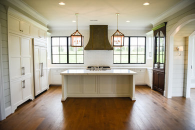 Example of a large farmhouse u-shaped medium tone wood floor and brown floor kitchen design in DC Metro with a farmhouse sink, beaded inset cabinets, white cabinets, solid surface countertops, white backsplash, cement tile backsplash, stainless steel appliances, an island and white countertops