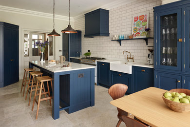 This is an example of a large transitional eat-in kitchen in Sussex with with island, a farmhouse sink, shaker cabinets, blue cabinets, white splashback, subway tile splashback, panelled appliances and beige floor.