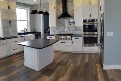 Design ideas for a mid-sized beach style l-shaped eat-in kitchen in Jacksonville with a farmhouse sink, shaker cabinets, white cabinets, soapstone benchtops, porcelain splashback, stainless steel appliances, vinyl floors, with island and black benchtop.