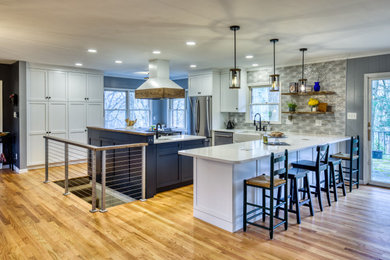 Example of a large minimalist u-shaped light wood floor and brown floor open concept kitchen design in Baltimore with a farmhouse sink, shaker cabinets, blue cabinets, quartz countertops, multicolored backsplash, ceramic backsplash, stainless steel appliances, two islands and white countertops