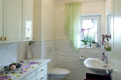 Mittelgroße Klassische Gästetoilette mit verzierten Schränken, weißen Schränken, Wandtoilette mit Spülkasten, farbigen Fliesen, Steinfliesen, beiger Wandfarbe, Marmorboden und Sockelwaschbecken in München