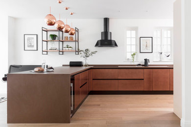 Eat-in kitchen - large industrial l-shaped eat-in kitchen idea in London with solid surface countertops, black appliances, a peninsula and brown countertops