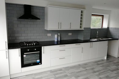 Inspiration for a large modern grey and white kitchen in Hampshire with a double-bowl sink, flat-panel cabinets, white cabinets, laminate countertops, grey splashback, ceramic splashback, black appliances, laminate floors, grey floors and black worktops.