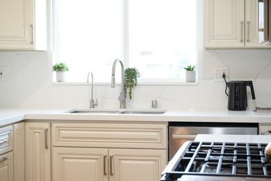 Mid-sized elegant galley light wood floor and brown floor eat-in kitchen photo in Los Angeles with a double-bowl sink, raised-panel cabinets, beige cabinets, quartz countertops, white backsplash, quartz backsplash, stainless steel appliances, a peninsula and white countertops