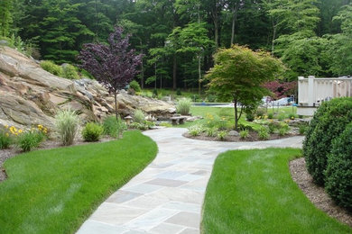 This is an example of a large traditional backyard full sun garden for spring in New York with with pond and natural stone pavers.