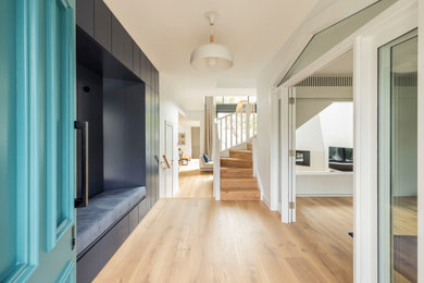 This is an example of a large modern entry hall in Sydney with white walls, light hardwood floors, a blue front door, brown floor, recessed and planked wall panelling.
