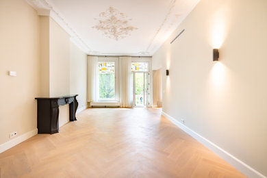 Modelo de salón contemporáneo con paredes beige, suelo de madera clara y marco de chimenea de piedra