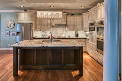 Mid-sized elegant l-shaped medium tone wood floor and brown floor eat-in kitchen photo in Nashville with an undermount sink, raised-panel cabinets, gray cabinets, granite countertops, white backsplash, subway tile backsplash, stainless steel appliances, an island and black countertops