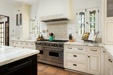 Inspiration for a large mediterranean u-shaped eat-in kitchen in Los Angeles with recessed-panel cabinets, beige cabinets, quartzite benchtops, white splashback, subway tile splashback, stainless steel appliances, with island, a farmhouse sink, terra-cotta floors, brown floor and white benchtop.