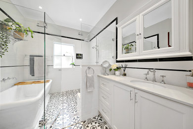 Large traditional master wet room bathroom in Sydney with shaker cabinets, white cabinets, a freestanding tub, a two-piece toilet, black and white tile, porcelain tile, grey walls, porcelain floors, an undermount sink, engineered quartz benchtops, black floor, a hinged shower door and white benchtops.