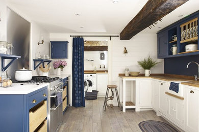 Design ideas for a beach style u-shaped separate kitchen in Wiltshire with a farmhouse sink, blue cabinets, wood benchtops, metallic splashback, stainless steel appliances, medium hardwood floors, no island and beige floor.