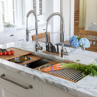 Große Klassische Küche in U-Form mit Vorratsschrank, Waschbecken, Schrankfronten mit vertiefter Füllung, weißen Schränken, Marmor-Arbeitsplatte, Rückwand aus Backstein, Elektrogeräten mit Frontblende, hellem Holzboden, Kücheninsel und grauer Arbeitsplatte in Charleston