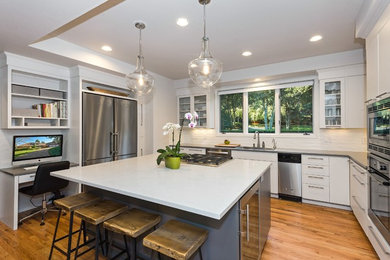 Example of a large transitional u-shaped medium tone wood floor enclosed kitchen design in Seattle with a drop-in sink, flat-panel cabinets, white cabinets, quartz countertops, white backsplash, subway tile backsplash, stainless steel appliances and an island
